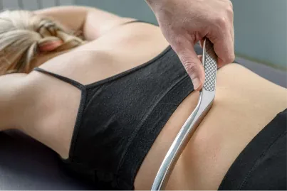 A stainless-steel Graston instrument worked along a patient's lower back