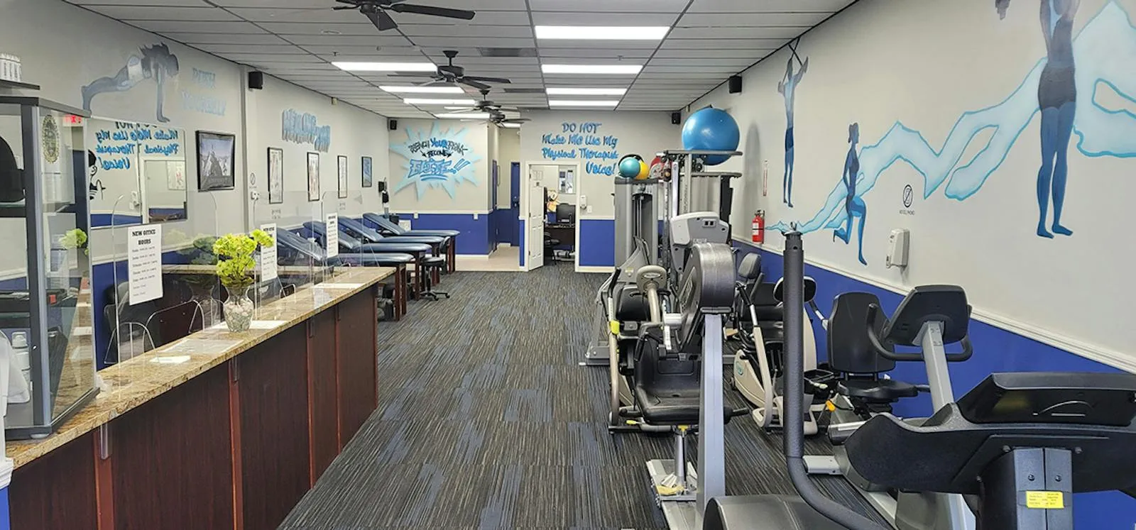 The long clinic floor, with the front counter on the left, exercise machines on the right and athlete murals on the walls